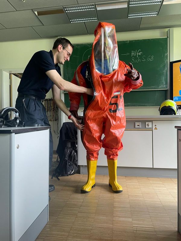 Physiklehrer Florian Rüther konnte sich vom Gewicht des Chemikalienschutzanzugs persönlich überzeugen, nachdem Oberbrandmeister Richard Dewitz beim Anziehen geholfen hatte. Fotos: Stadt Marl